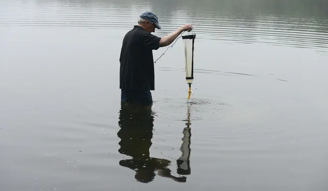 Bill Wood fills a skim net that is dragged across the water surface at Pine Pond in Brewster to collect a sample that will be tested for cyanobacteria. Wood volunteers with the Brewster Ponds Coalition, which samples 19 ponds in the town.