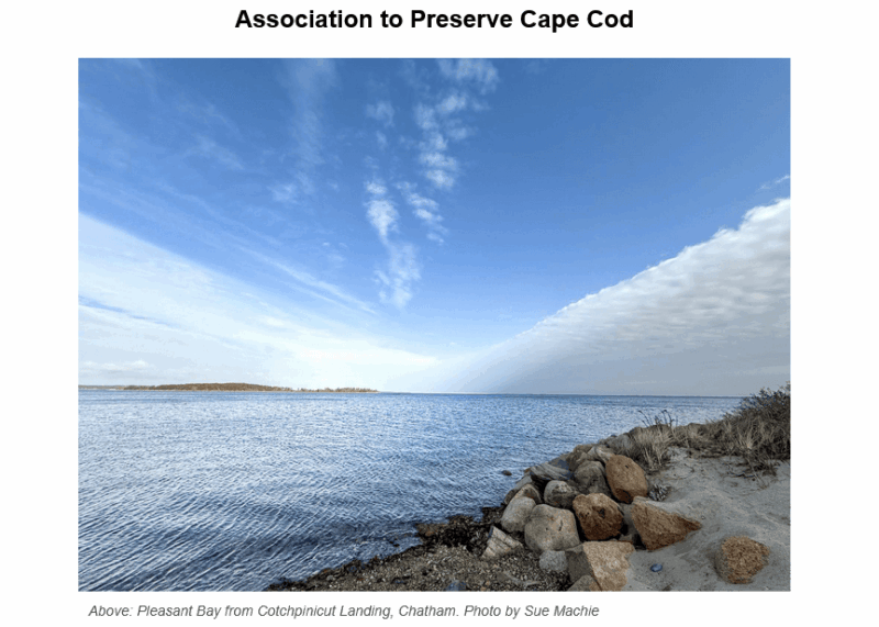 Scenic view of Pleasant Bay from Cotchpinicut Landing in Chatham, showing calm blue water, rocky shoreline with beach grass, and distant land under a partly cloudy sky
